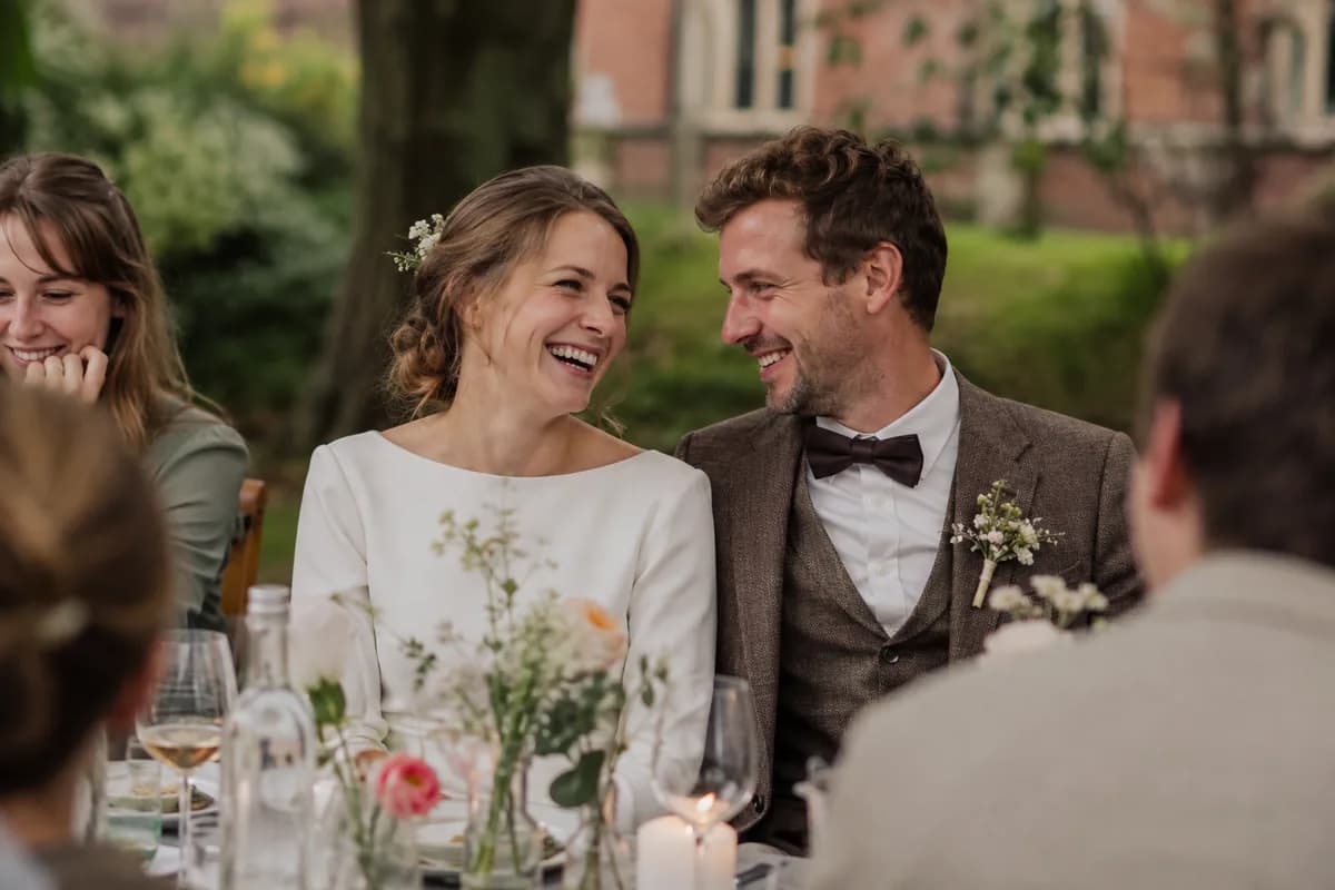 Newlyweds laughing with their guests at the wedding reception table